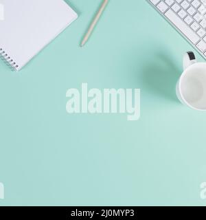 Close up blank notepad pencil cup keyboard turquoise background with space text Stock Photo