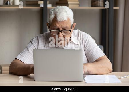 Serious older man sit at table use laptop Stock Photo