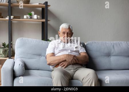 Thoughtful older man sits alone on sofa lost in thoughts Stock Photo