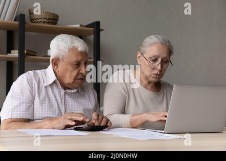 Serious aged spouses sit at desk manage household finances Stock Photo