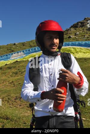 A Indian young male tourist opening bottle cap for drink water before taking paragliding flight in the mountain Stock Photo