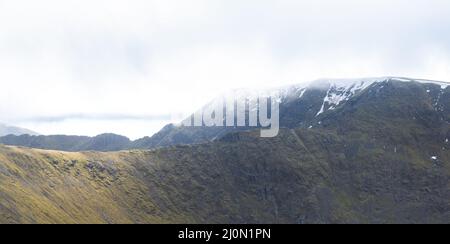 The snow capped peak of Helvellyn in the Lake District, with Swirral Edge and Striding edge visible in the backround, UK Stock Photo