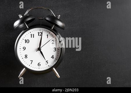Alarm clock showing 5 o clock against black background Stock Photo