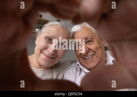 Older couple looking through their joined fingers showing heart shape Stock Photo