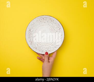 Female hand holding an empty round plate on a yellow background, top view Stock Photo