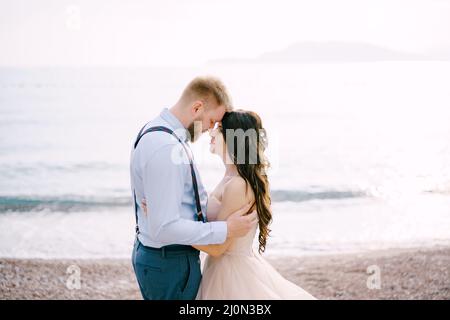 The bride and groom stand on the pebbled seashore and hug Stock Photo