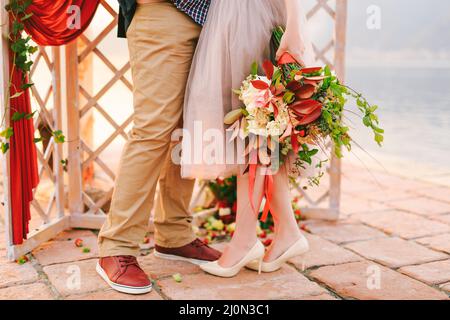 Groom and bride with a bouquet of flowers stand on a stone tile against the background of a carved screen decorated with a red c Stock Photo