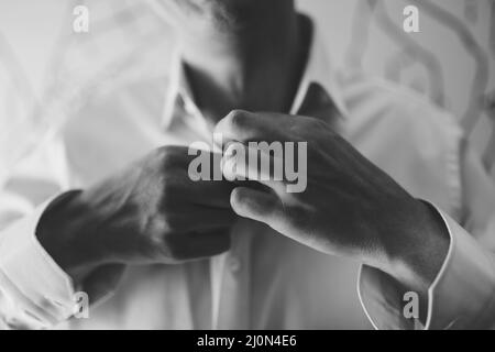 Man is buttoning the buttons on a white shirt. Close-up. Black and white photo Stock Photo