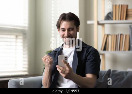 Joyful happy smartphone user guy getting exciting good news Stock Photo