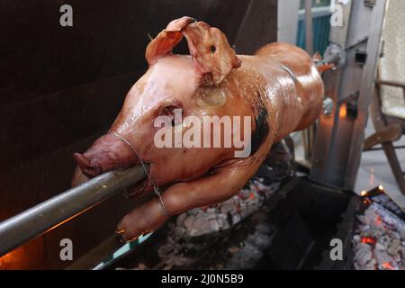 Pig is being grilled slowly on spit in traditional way, cooked with charcoal, fatty roasted meat Stock Photo