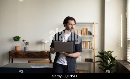 Pensive serious millennial business man standing at workplace table Stock Photo