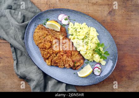 Traditional deep-fried schnitzel with potato salad and lemon slices served as top view on a modern Nordic design plate with copy Stock Photo