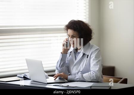 Busy serious mature female chief doctor speaking on mobile phone Stock Photo