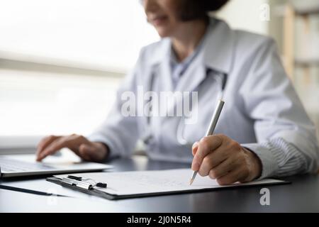 Hands of mature doctor woman filling paper medical records Stock Photo