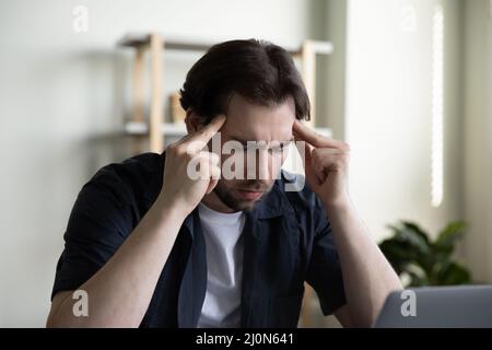 Stressed focused millennial businessman with closed eyes touching head Stock Photo