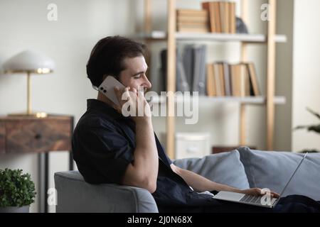 Happy positive young entrepreneur man resting on sofa, using gadgets Stock Photo