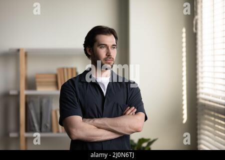 Thoughtful serious young businessman in casual standing at window Stock Photo