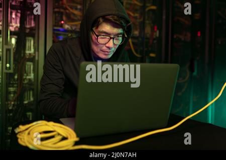 Asian male hacker using a laptop in computer server room Stock Photo