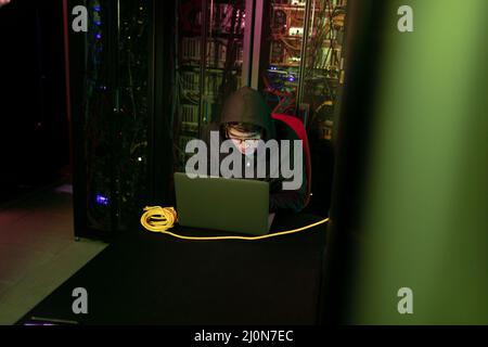 Asian male hacker using a laptop in computer server room Stock Photo