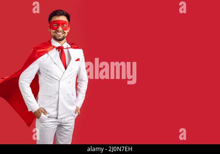 Happy handsome superman in suit, mask and cape standing on red copy space background Stock Photo