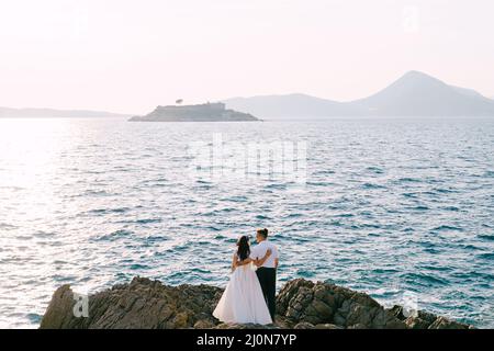 Bride and groom are embracing on the rocks and looking at each other. Back view Stock Photo