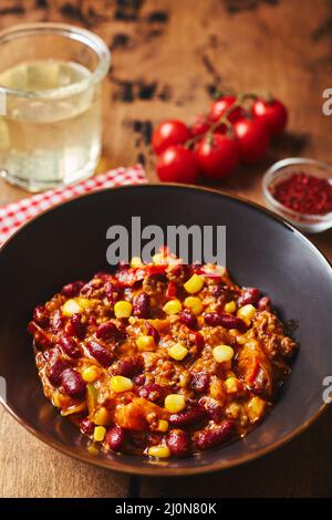 Chili Con Carne with ground beef, beans and corn in dark bowl on wooden background. Mexican and Texas cuisine Stock Photo