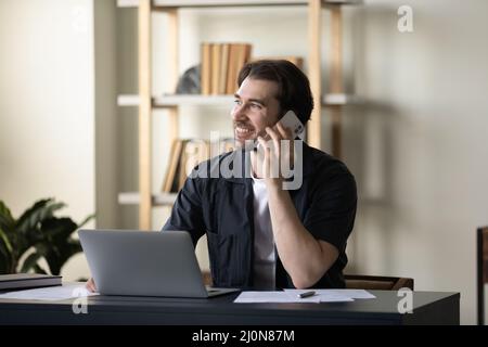 Happy handsome millennial businessman making phone call to client Stock Photo