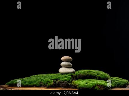 Stack of round stones on green moss, black background. Podium to showcase products, cosmetics and items, advertising Stock Photo