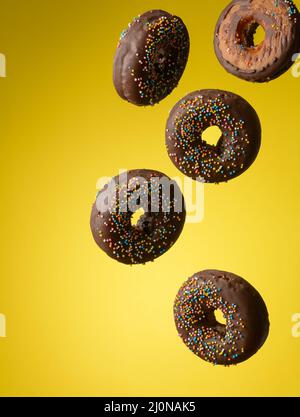 Chocolate round donuts with multicolored sugar sprinkles levitate on a yellow background Stock Photo