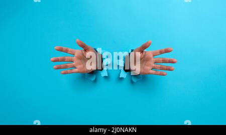 Two female palms sticking out of a torn hole in blue paper Stock Photo