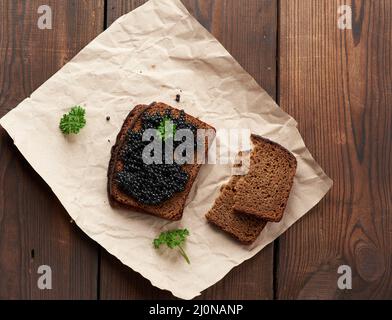 Fresh grainy black paddlefish caviar in brown wooden spoon on a brown table Stock Photo