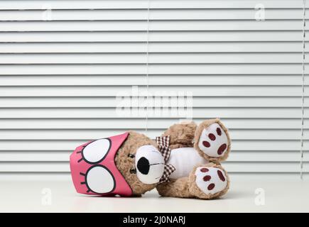 Brown teddy bear sits with a bandage for sleeping on a white table Stock Photo