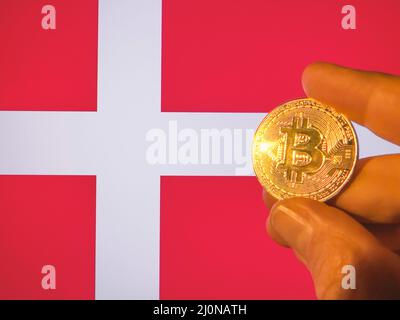 Holding a physical golden Bitcoin over the Danish flag. Denmark as cryptocurrency and blockchain technology investor. Financial background