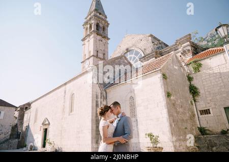 Groom hugs bride on the stone square in front of the church Stock Photo