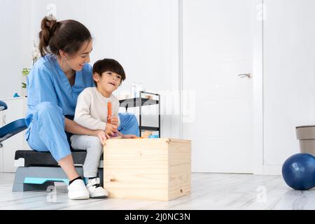 Therapist doing development activities with a little boy with with cerebral palsy, having rehabilitation, learning . Training in Stock Photo