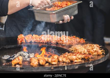 Preparing chicken meat skewers, grilled or roasted in a barbecue on an open fire and flames, shashlik or shashlyk for a picnic with pitchforks, close Stock Photo