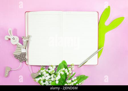 Notepad for text with pen. Bouquet of lilies of valley and rabbits on pink background. Easter. Copy space Stock Photo
