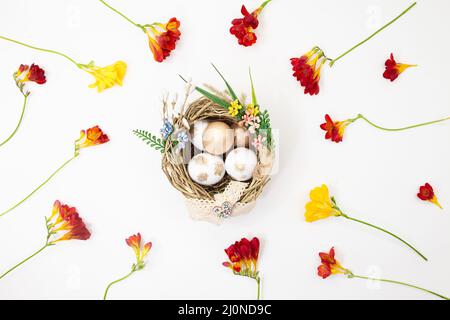 Nest with white and golden eggs in nest with yellow and red flowers on white background. Easter. Copy space Stock Photo