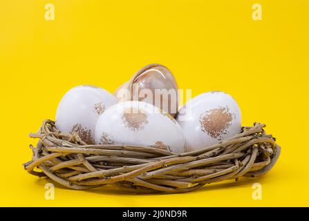 Nest with white eggs with gold on yellow background. Easter. Copy space Stock Photo