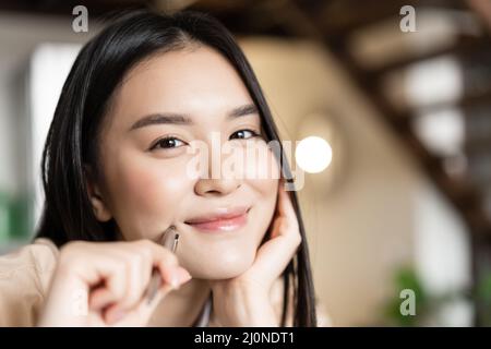 Portrait of smiling asian woman face looking happy, holding pen and grinning, working or doing homework Stock Photo