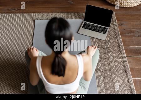Mindfulness and meditation concept. Rear view of young asian woman meditating at home, following online course on laptop, sittin Stock Photo