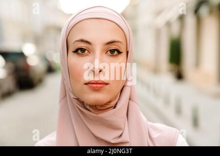 Close up of a smiling young muslim woman in hijab standing on a street looking at camera Stock Photo