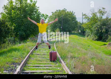 in a yellow jacket, a tourist with a suitcase jumps on the railroad Stock Photo