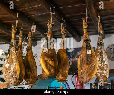 Aracena, Spain - 16 March, 2022: legs of Iberico ham from Jabugo hanging from the ceiling in a traditional countryside inn and restaurant Stock Photo