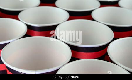 Row of red and black disposable eco friendly paper cup for coffee or hot beverage on dark backdrop. Selective focus. Close-up. Stock Photo