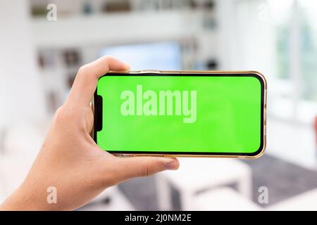 Hand in modern living room via smart home on mobile phone with blank green screen Stock Photo