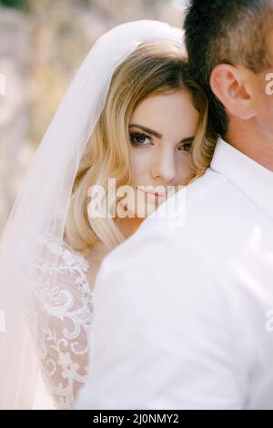 Bride in the white dress is leaning against the groom shoulder from behind. Portrait Stock Photo