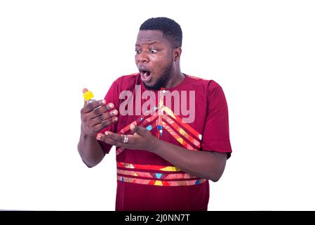 a handsome man wearing a loincloth shirt standing on a white background looks at bottle of liquor with surprised air. Stock Photo