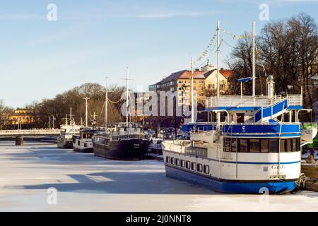 Bar boats moored on the frozen Aura River at cold sunny winter day in Turku. Finnish winter landscape. Stock Photo