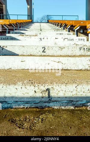 Numbered steps in the sport stadium between the wooden seats over the blue sky. Concrete stairs at the empty stadium without the spectators Stock Photo
